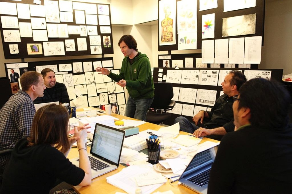 A photo of a team at Pixar discussing a movie, surrounded by storyboards